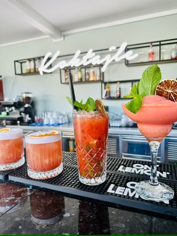 Drei Cocktails unter dem Cocktails-Neon — bordeauxrote Sours auf der Bar Mat